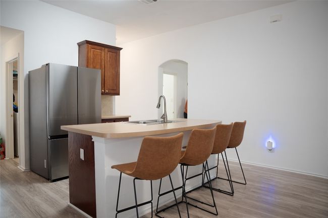 Kitchen with freestanding refrigerator, a sink, light wood-style flooring, arched walkways, and a kitchen island with sink | Image 7