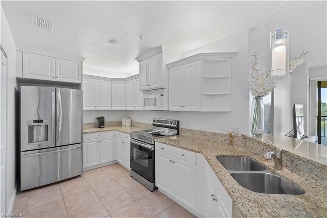 Kitchen with sink, white cabinetry, light tile patterned floors, light stone countertops, and stainless steel appliances | Image 6