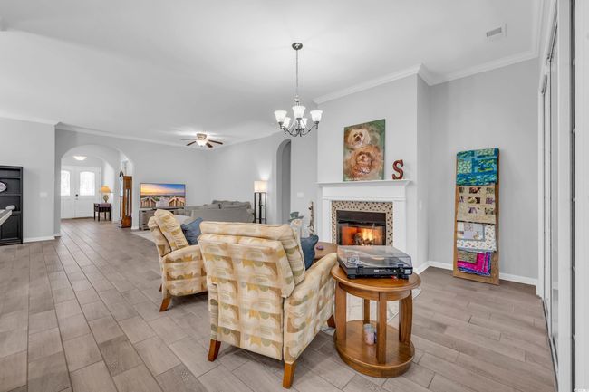 Living room with a fireplace, wood finished floors, ornamental molding, arched walkways, and ceiling fan with notable chandelier | Image 18