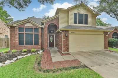 This is a two-story brick house featuring a prominent arched entryway, large front windows with grids, and an attached two-car garage. The property includes a landscaped front yard with a brick walkway and mature trees around. | Image 3