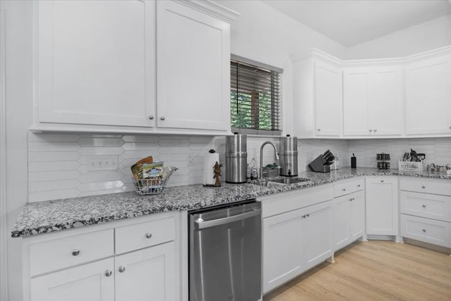 Kitchen with white cabinetry, stainless steel dishwasher, backsplash, and a sink | Image 14