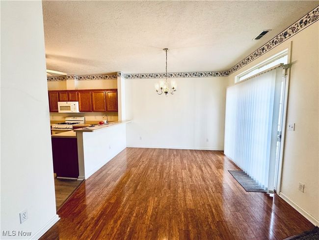 Unfurnished dining area featuring an inviting chandelier, a textured ceiling, wood finished floors, and baseboards | Image 4