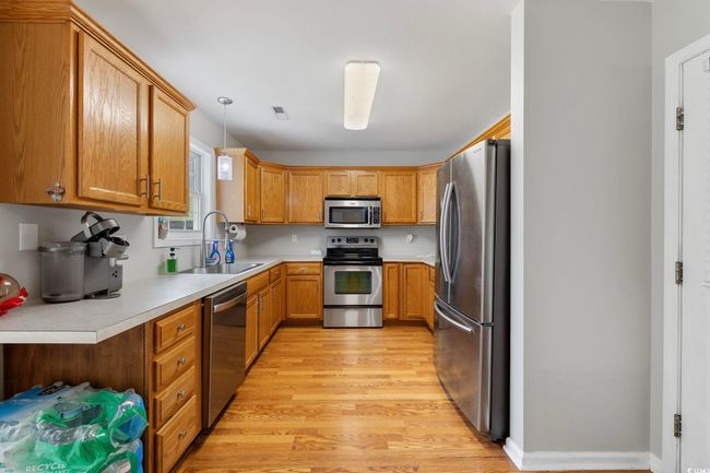 Kitchen featuring appliances with stainless steel finishes, a sink, light wood-style flooring, light countertops, and hanging light fixtures | Image 28