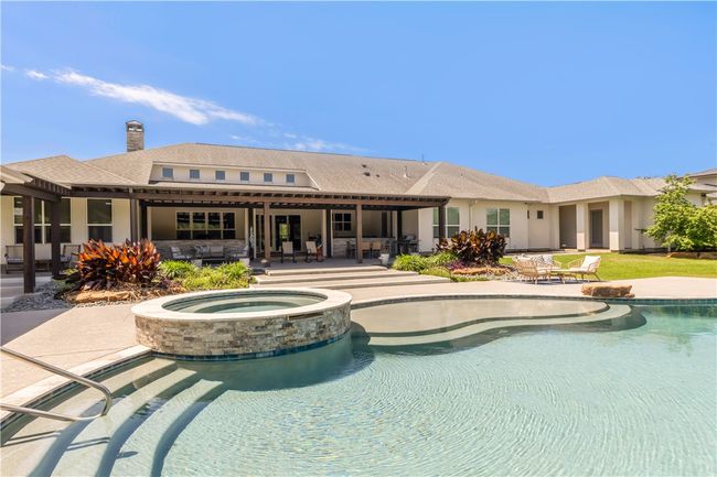 Back of house featuring a patio area, a pool with connected hot tub, an outdoor living space, and a chimney | Image 22