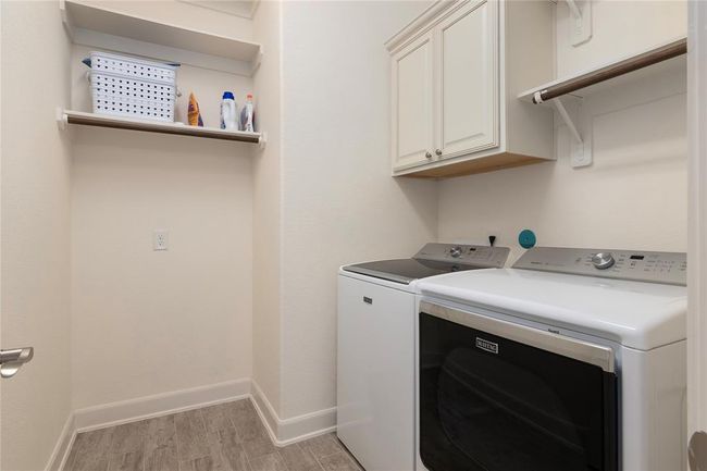 This photo shows a well-organized laundry room. There are overhead cabinets for storage and a shelf for additional items, all set against the neutral walls and flooring, creating a clean and functional space. | Image 19