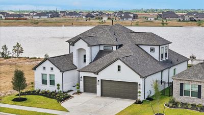 This is a modern two-story home with a white exterior and gray roof, featuring a three-car garage and a well-landscaped front yard. The house is located in a new development with a waterfront view, offering a serene setting. | Image 2