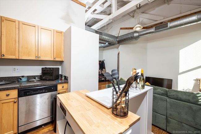 Modern-industrial kitchen with exposed brick walls, high ceilings, and large windows allowing ample natural light, featuring wooden cabinetry and stainless steel appliances | Image 9