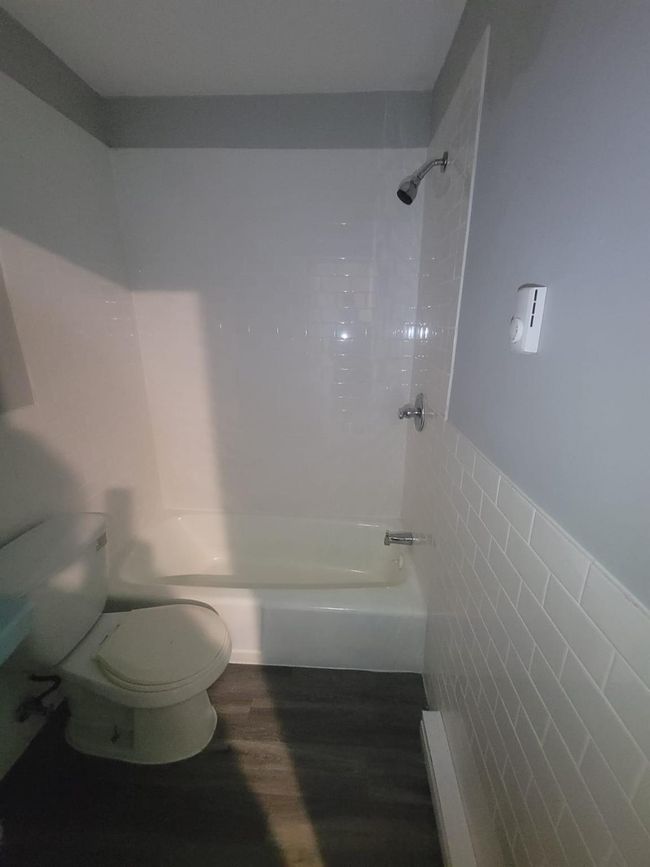 Full bath featuring toilet, wood finished floors, shower / bathtub combination, tile walls, and a wainscoted wall | Image 4