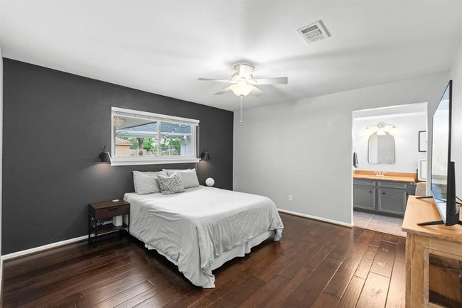 The bright and spacious primary bedroom features a dark accent wall, hardwood floors, and a ceiling fan. It includes a large window for natural light and an en-suite bathroom with modern fixtures. | Image 17
