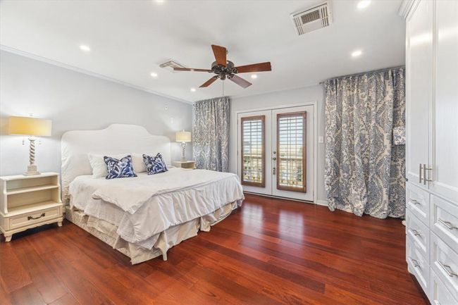 This spacious primary bedroom features elegant wood flooring and ample natural light from French doors. It includes built-in storage, a ceiling fan, and tasteful decor for a comfortable, inviting atmosphere. | Image 24