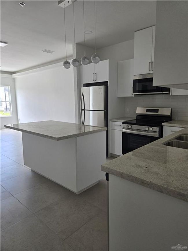 Kitchen with appliances with stainless steel finishes, backsplash, a center island, white cabinets, and hanging light fixtures | Image 4
