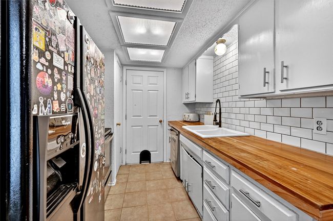 Kitchen featuring appliances with stainless steel finishes, wooden counters, decorative backsplash, light tile patterned flooring, and a textured ceiling | Image 9