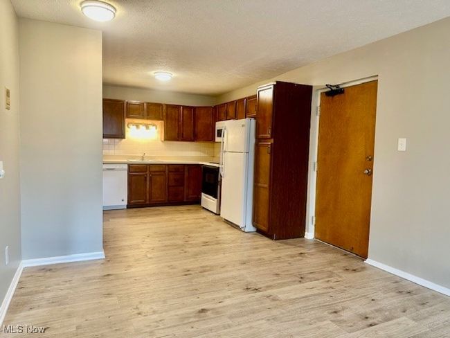 Kitchen with white appliances, a sink, light countertops, light wood-style floors, and tasteful backsplash | Image 8