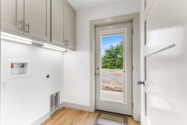 Washroom featuring cabinet space, hookup for an electric dryer, light wood finished floors, baseboards, and hookup for a washing machine | Image 28
