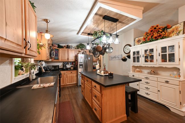 Kitchen featuring stainless steel fridge, dark countertops, a sink, dark wood-type flooring, and glass insert cabinets | Image 23