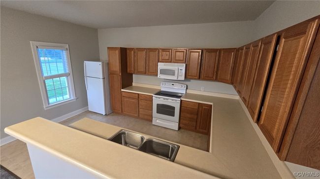 Kitchen with a sink, white appliances, brown cabinets, light countertops, and baseboards | Image 43