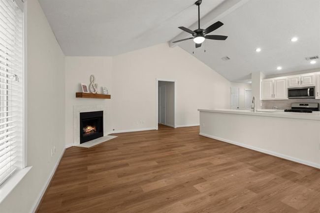 Fresh paint throughout, modern vinyl plank flooring, updated ceiling fan and lighting, and a beautifully retiled fireplace creating a warm focal point. | Image 12