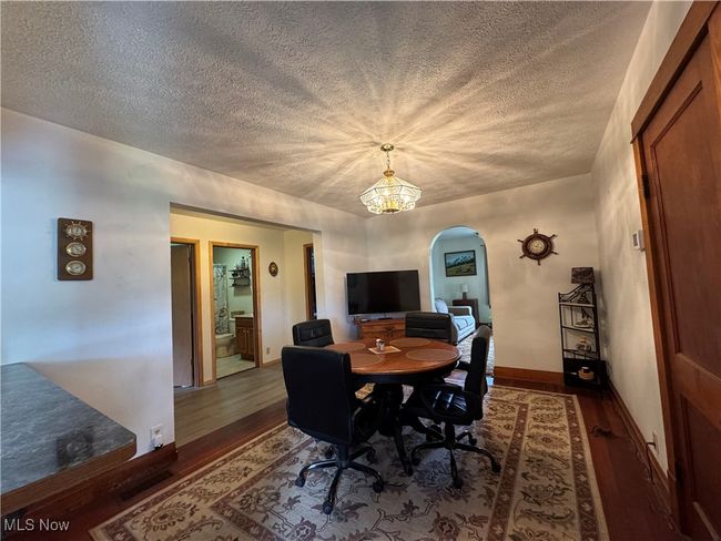 Dining area featuring arched walkways, a textured ceiling, wood finished floors, a chandelier, and baseboards | Image 12