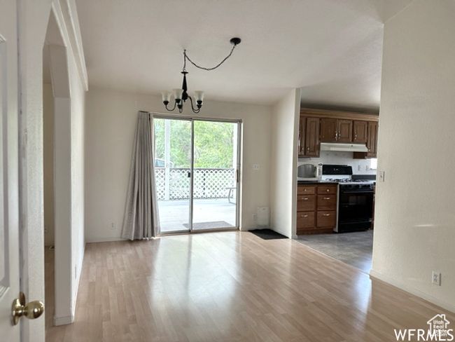 Kitchen with a notable chandelier, light wood-type flooring, under cabinet range hood, range with gas cooktop, and white microwave | Image 12