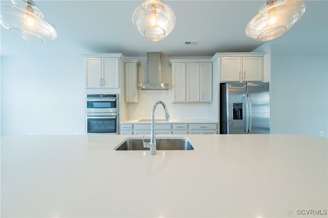 Kitchen featuring stainless steel appliances, wall chimney range hood, a sink, light countertops, and pendant lighting | Image 17