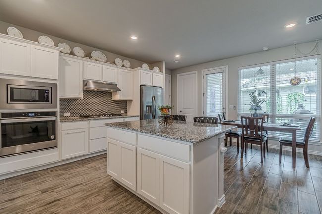 Kitchen with stainless steel appliances, range hood, wood finished floors, a center island, and decorative backsplash | Image 13