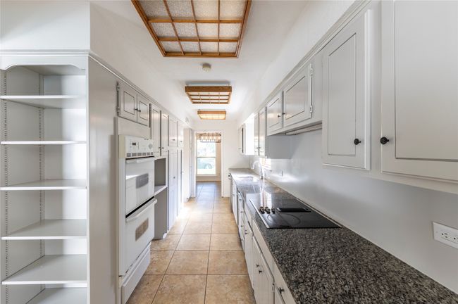 Kitchen features stainless double sink, open shelves, light tile patterned floors, and black electric cooktop | Image 13