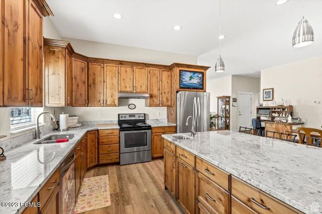 Kitchen featuring stainless steel appliances, under cabinet range hood, brown cabinets, light wood-type flooring, and light stone countertops | Image 7