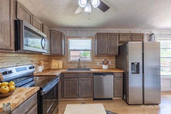 Kitchen with stainless steel appliances, a sink, wood counters, a ceiling fan, and wooden walls | Image 4