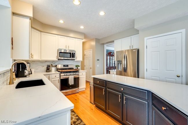 Kitchen featuring stainless steel appliances, tasteful backsplash, white cabinetry, a textured ceiling, and light wood-type flooring | Image 8
