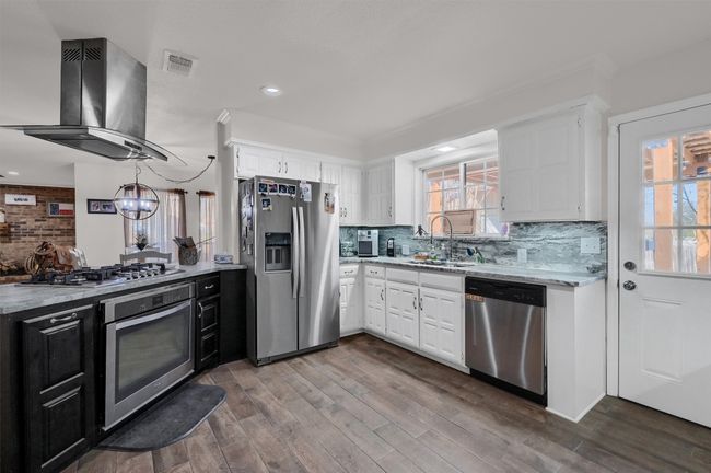 Kitchen featuring dark cabinetry, appliances with stainless steel finishes, tasteful backsplash, ventilation hood, and white cabinets | Image 9