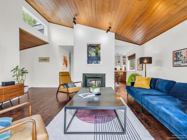 Spacious open concept living Room with vaulted warm wood ceiling, full height west facing (new) windows flooding the room with natural light, and a cozy gas fireplace as a central focal point in the 'Great Room'. | Image 9