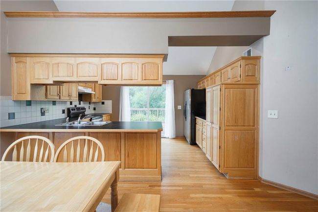 Kitchen with stainless steel appliances, light wood-style floors, a peninsula, decorative backsplash, and vaulted ceiling | Image 12