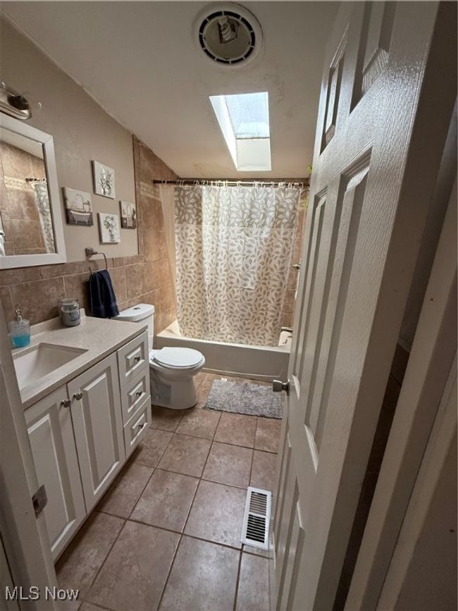 Full bathroom featuring a skylight, shower / bath combination with curtain, toilet, tile patterned flooring, and visible vents | Image 18