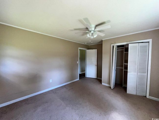 Unfurnished bedroom with baseboards, carpet, crown molding, a closet, and a ceiling fan | Image 9