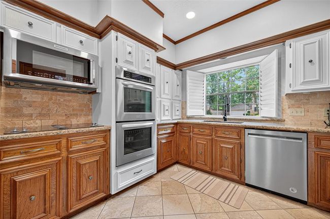 Abundant cabinetry above and below offers ample storage in the kitchen, while a complementing backsplash and oversized window bring character and natural light to this well-equipped space. | Image 19