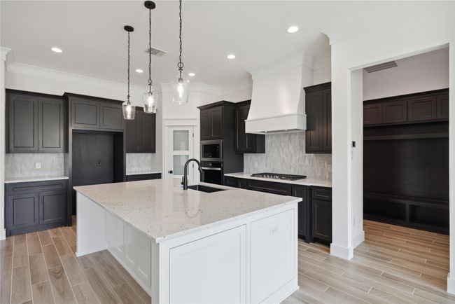 Kitchen featuring custom exhaust hood, a kitchen island with sink, light stone counters, stainless steel appliances, and crown molding | Image 19