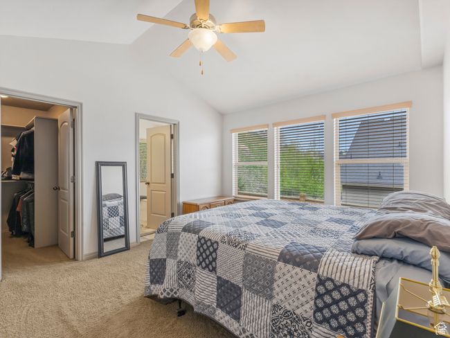 Bedroom featuring a walk in closet, light colored carpet, vaulted ceiling, a closet, and ceiling fan | Image 16
