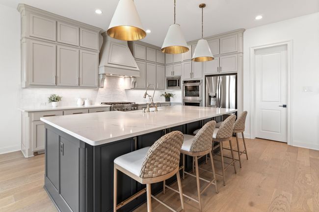 Kitchen with gray cabinetry, light wood-style flooring, decorative backsplash, decorative light fixtures, and a center island with sink | Image 11