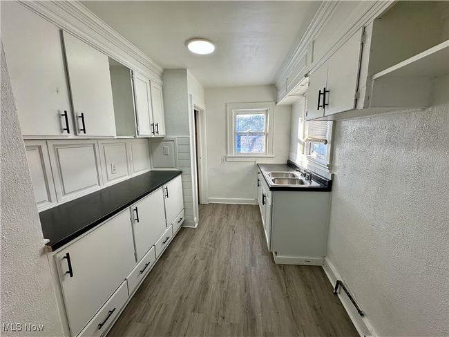 Kitchen with white cabinets, dark countertops, a sink, baseboards, and dark wood-style flooring | Image 6