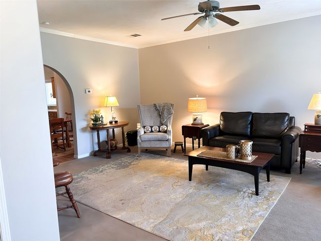 Living room with visible vents, baseboards, ceiling fan, ornamental molding, and arched walkways | Image 13