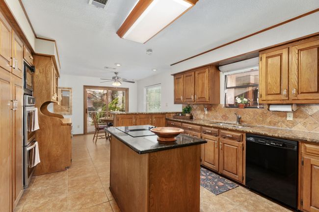 Kitchen with brown cabinets, tasteful backsplash, a sink, black appliances, and a peninsula | Image 18