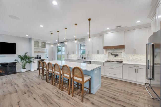 Kitchen with light countertops, white cabinets, a breakfast bar, stainless steel appliances, and premium range hood | Image 11