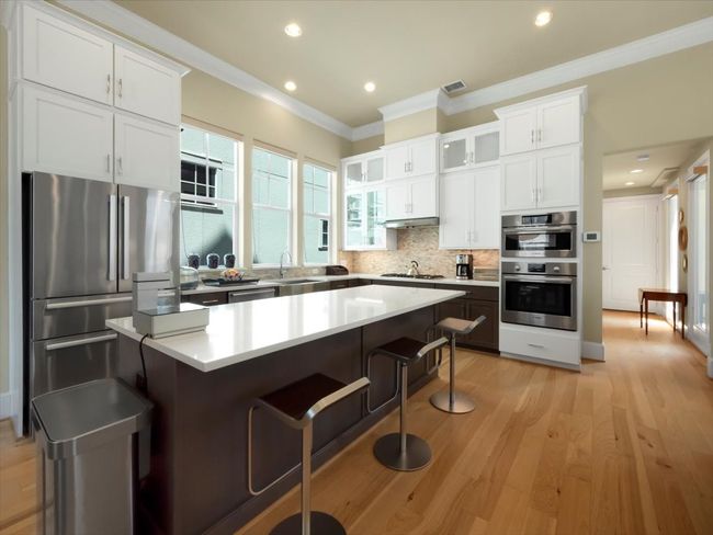 Kitchen featuring appliances with stainless steel finishes, crown molding, a kitchen bar, white cabinetry, and decorative backsplash | Image 6