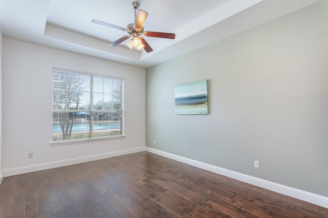 Unfurnished room with dark wood finished floors, baseboards, a tray ceiling, and a ceiling fan | Image 16