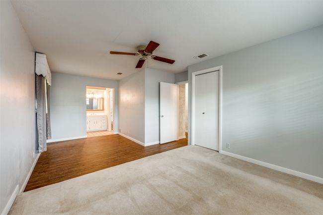 Unfurnished bedroom featuring carpet flooring, baseboards, ceiling fan, ensuite bathroom, and wood finished floors | Image 18