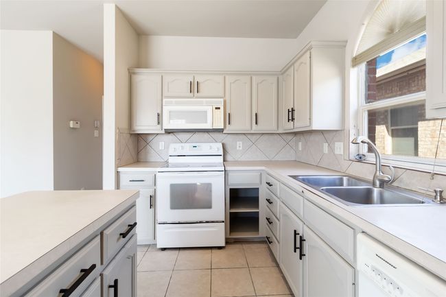 Kitchen featuring tasteful backsplash, light countertops, light tile patterned flooring, white appliances, and a sink | Image 20