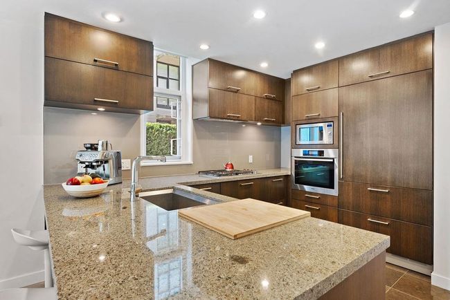 Kitchen with a peninsula, light stone countertops, modern cabinets, appliances with stainless steel finishes, and a large sized sink | Image 25