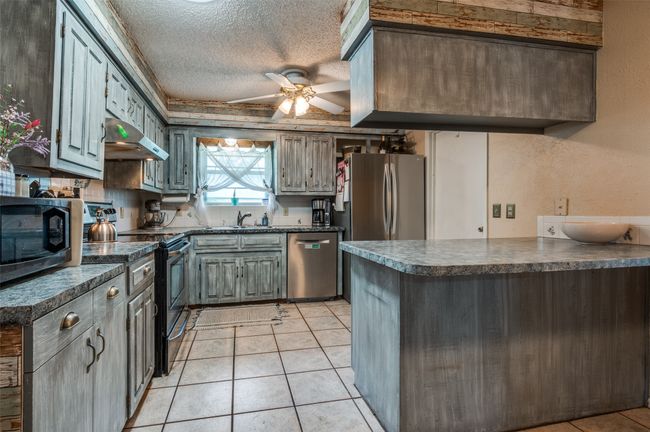 Kitchen featuring dark countertops, a textured ceiling, stainless steel appliances, a ceiling fan, and a peninsula | Image 4