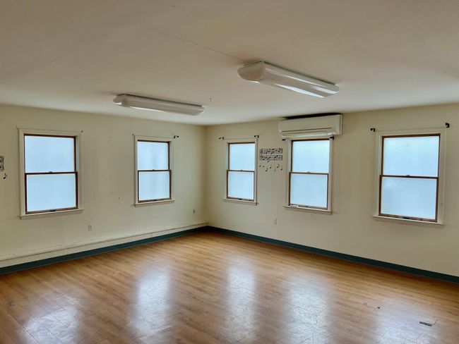 Empty room with baseboard heating, wood finished floors, a wall mounted air conditioner, and baseboards | Image 12