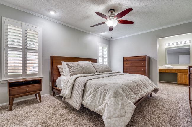 Bedroom with light colored carpet, crown molding, a textured ceiling, a ceiling fan, and ensuite bathroom | Image 15